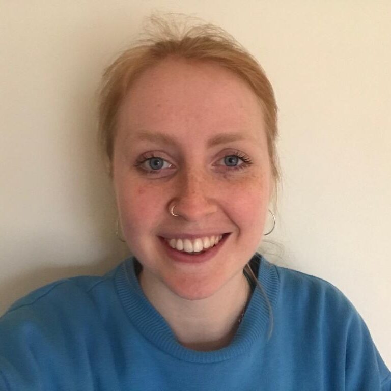 Georgie: Picture shows a women with auburn hair smiling. She is wearing a nose ring and blue sweater