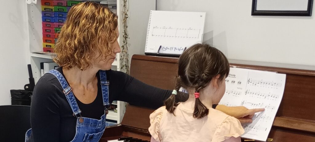Woman pointing at sheet music while a young girl is playing the piano.