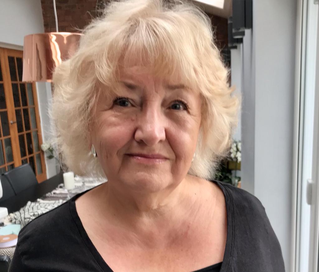 Pat: picture shows a women with short blonde wavy hair smiling. She is wearing a black top