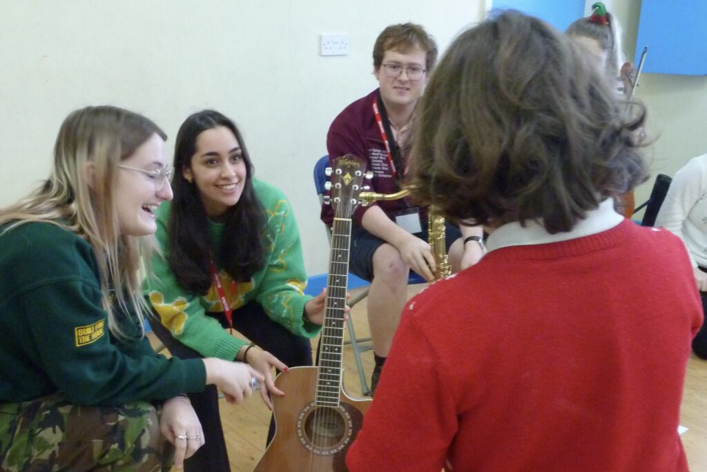 Three students showing a young boy a guitar. 